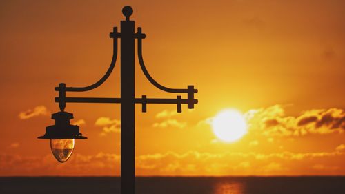 Silhouette street light by sea against orange sky