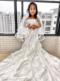 Portrait of girl wearing wedding dress by window at home