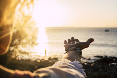 Cropped hand of woman gesturing at beach against sea and sky during sunset