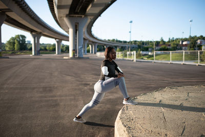 African american runner lunging under bridge