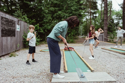 Full length of woman playing miniature golf with family in backyard