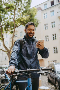 Smiling food delivery person using smart phone while holding bicycle