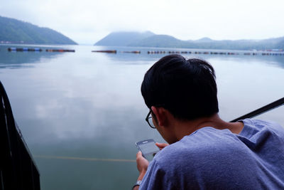 Rear view of man using mobile phone in lake