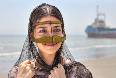 Close-up of young woman wearing traditional clothing standing at beach against sky