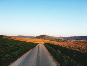 Road amidst field against clear blue sky