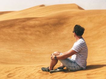Side view of young man sitting on sand