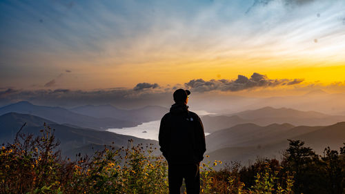 Rear view of man standing on mountain against sky during sunset