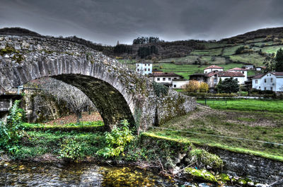 Arch bridge over river amidst buildings against sky