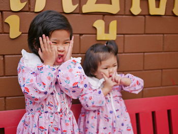 Cute girls making face standing against wall outdoors