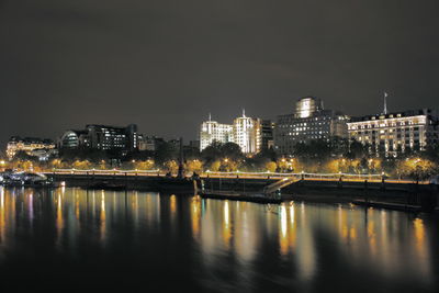 Thames river by illuminated buildings against sky