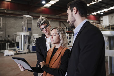 Young businesswoman discussing over tablet pc with colleagues at industry