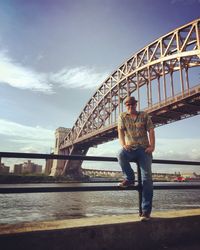 Full length portrait of man leaning on railing against hell gate bridge