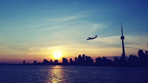 Scenic view of sea by silhouette cityscape against sky during sunset