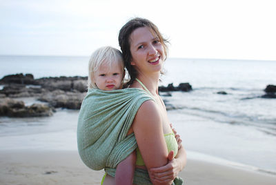 Young woman carrying baby on back standing at beach