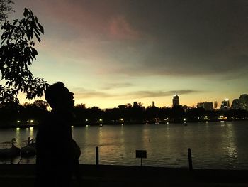 Silhouette trees by river against sky during sunset