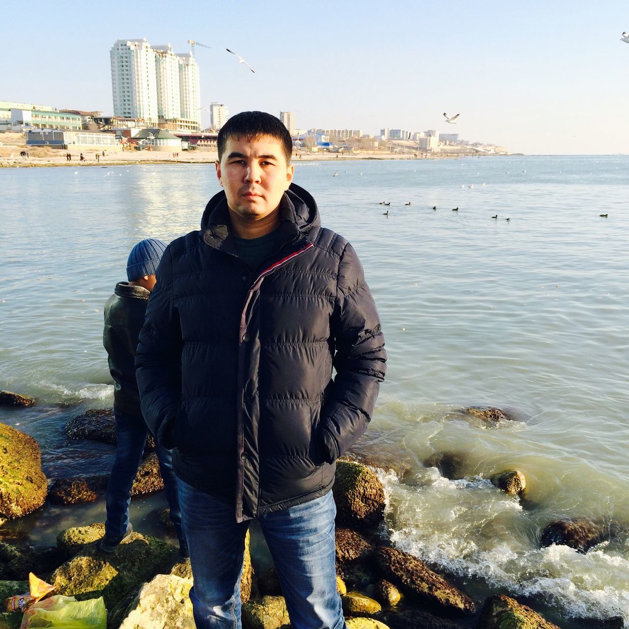 water, looking at camera, casual clothing, standing, lifestyles, sea, person, portrait, leisure activity, young men, young adult, beach, front view, three quarter length, full length, smiling, shore, sky