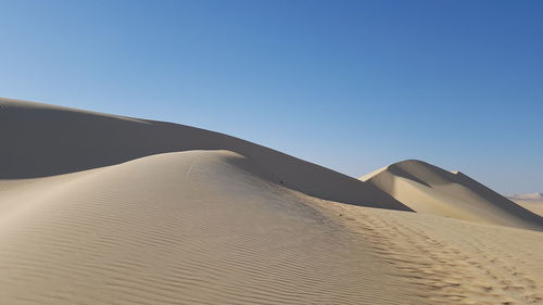 Low angle view of sand dunes against clear blue sky