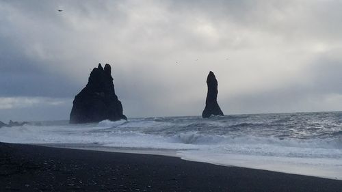 Silhouette rocks on beach against sky