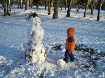 Side view of boy standing by snowman in forest