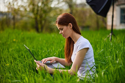 Young woman using mobile phone while sitting on field