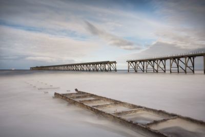 Bridge over sea against cloudy sky