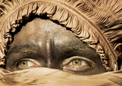 Close-up portrait of a woman's face, green eyes in golden colored head scarf