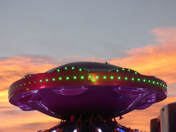 Low angle view of illuminated carousel against sky at sunset