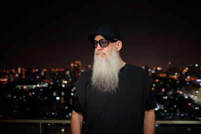 Portrait of man wearing sunglasses standing against illuminated city at night