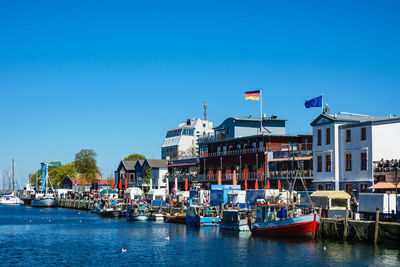 Boats moored at harbor against clear blue sky