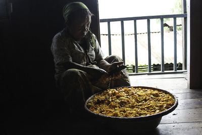 Mature woman preparing food while sitting by entrance at home