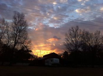 Bare trees against cloudy sky at sunset