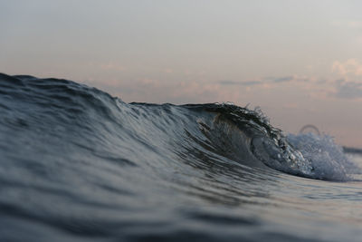 Close-up of wave splashing on beach against sky during sunset