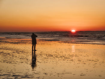 Silhouette woman on beach against sky during sunset