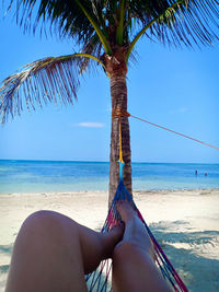 Low section of woman relaxing in hammock at beach