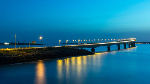 Bridge over sea against blue sky at night