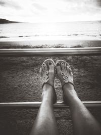 Low section of woman on sea shore against sky
