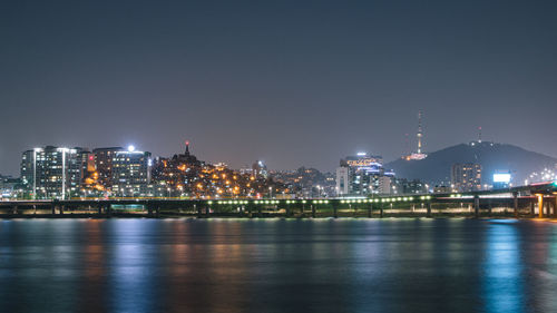 Illuminated city by river against sky at night