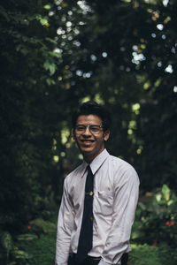 Portrait of smiling young man standing against trees in park