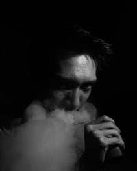 Portrait of young man smoking over black background