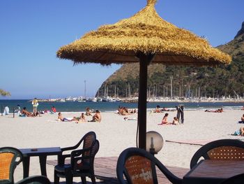 Thatched roof and chairs against people relaxing at beach