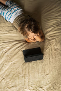 Boy lying on the bed using digital tablet computer playing games or watching cartoons at home.