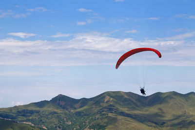 Person paragliding over mountains against sky