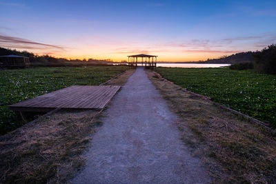 Walkway amidst field against sky during sunset