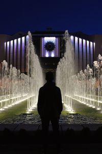 Rear view of silhouette man standing against illuminated building