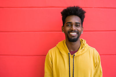 Portrait of smiling young man standing against red wall