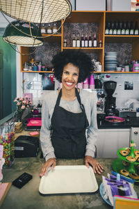 Portrait of happy female barista with serving tray in cafe