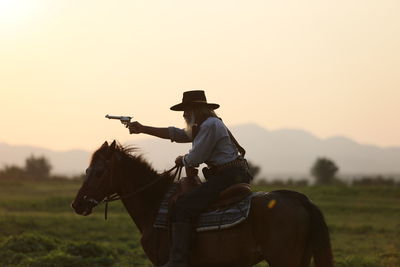 Man riding horse while shooting with handgun against sky