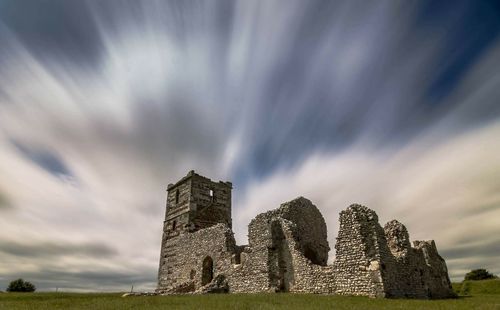 Old ruins on grassy field against cloudy sky