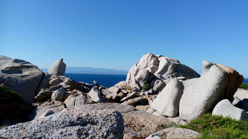 Rocks by sea against clear blue sky