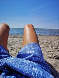 Low section of man relaxing at beach on sunny day